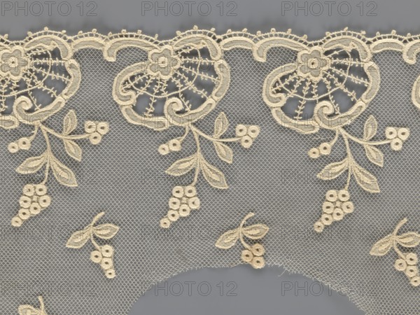 Fragment of lace, lace with plant ornaments, slightly serrated lower edge, featuring shell motifs with sprouting twigs and projections of smaller twigs above, 2nd half of the 19th century, Europe, width 20 cm, length 161 cm, A delicate lace fabric with an overall beige embroidery set against a gray background, showing a scalloped top edge with ornate floral motifs and looping embroidered outlines, a fine diamond mesh net filling the spaces, and several hanging sprigs of embroidered leaves and small clustered round flower-like shapes; the visible colors are beige and gray.