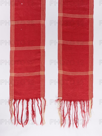 Belt; woolen; red with motifs of three narrow cream-colored trails spaced lengthwise and crosswise every 20–25 cm; fringes at both ends created from warp threads; 19th century; Poland; length 400 cm; width 29.5 cm; men's clothing accessory; geometric ornaments; Polish clothing., The image shows two long woven fabric panels hanging vertically against a light background; both panels are predominantly red with a pattern of lighter stripes forming rectangular grids and both end in a fringe of loose threads; the fringes contain red and lighter colored threads, and the fabric surface shows slight texture and small imperfections.