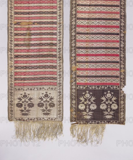 Kontusz sash, Paschalis Jakubowicz Manufactory Warsaw; belt manufacturer; 1788-1794. Solid kontusz sash, double-sided. Bipartite heads with a flower bush pattern. Alternating transverse stripes, plain and with geometric ornamentation. Edge with a floral tendril motif. Colors: gold, silver, blue, yellow-green, light red, brown, light blue. Sew-on fringe, silver, with gaps. Ornament - Heads: two motifs of rooted flower bushes. - Center: alternating transverse shelves, smooth and with rhombus motifs. - Borders: vertical and horizontal with different floral tendril motifs; checkerboard and rhombus. Colors placement - Front: background of heads, borders and smooth shelves silver, ornament brown; background of the shelves with rhombuses alternating red and brown, silver ornament. - Reverse right: only smooth shelves alternating red and brown. Signed in the heads: Pascha/Nov. Weave density: approx. 19/34 x2. Date: 1788–1790. Place of origin: Lipków, Warsaw . Function: national costume accesso...