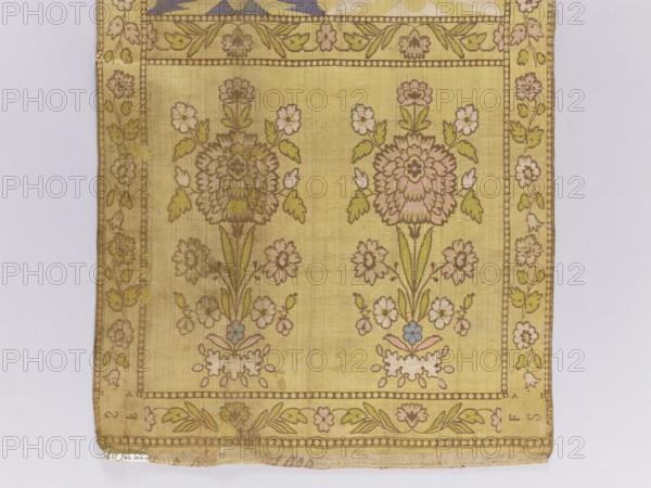 Kontusz belt, Bipartite heads with elongated floral bouquets; transverse belts with a floral tendril ornament alternating with geometric bands of elongated rosettes; floral tendril border. Floral ornaments, plant ornaments, floral tendrils. Colors: straw, cream, pink, sky blue, green, white, and navy blue. Signed at the bottom in the heads: FS lying. At the bottom edge of one end, an illegible inscription 1000?. 2nd half of the 18th century, Kraków, Polish national costume accessory. Length 357 cm, width 36.5 cm., A rectangular textile panel with a pale yellow background featuring a symmetrical floral pattern in muted colors; a pair of large stylized flower bouquets sit side by side, each rendered in shades of pink and beige with green leaves and stems, surrounded by smaller flowers in pale pink, white, and touches of light blue. The panel is bordered by a decorative band with repeating floral motifs and leaf elements in green, pink, and beige, and the edges show a narrow darker outlin...