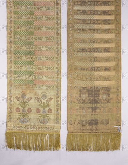 Kontusz sash, Bipartite heads with the pattern of flower bouquets on a vase-base, alternating transverse stripes with an ornament of floral tendrils and dots. Ribbon made of waxflower. Colors: brown, blue, red, green, and ochre. Signed at the bottom in the heads: FS lying. Late 18th century, Kraków. National costume accessory. Length 370 cm, width 35 cm. Materials/ornament: flower bouquets, flower bushes, szelagki, geometric and plant ornaments; four-sided sash; men's clothing accessory; Polish sash kontusz sash., Two long narrow fabric panels hang side by side with fringed bottoms in a gold-yellow color. The left panel shows horizontal bands of patterned stripes in pale green, soft pink, and cream, separated by thin floral vine motifs; a border with small floral and bird motifs runs along its edges. Near the lower portion of the left panel are stylized floral bouquets in muted blue, pink, green, and cream above a small floral border. The right panel has a similar striped layout but ap...