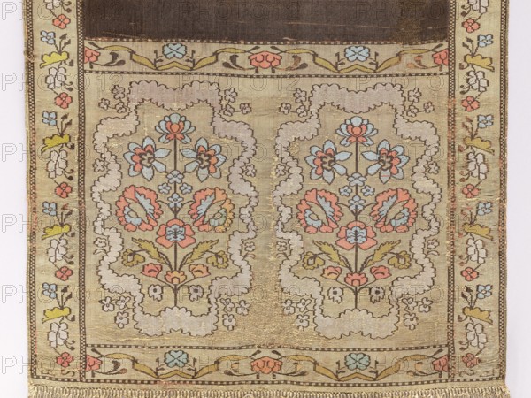 Kontusz belt, flower bushes ornament, bilateral belts, semi-solid belts, geometric ornaments, plant ornaments, Polish belts, Polish costumes, kontusz belts, belts, national costumes, signatures. On one side the background is brown-gray-black with gold dots; on the other a blue background with gold dots. Silver-gold, bipartite heads with floral bouquets enclosed in a wavy line around them. Bouquet colors: crimson, blue, and green. Signed in the heads: FS lying down. 18th century, Poland; national costume, clothing accessory. Length 291 cm, width 31 cm., A woven textile with a symmetrical floral pattern featuring a central pair of mirrored medallions, each filled with stylized flowers and leaves; the design uses colors including beige, light blue, pale pink, soft coral, muted yellow, olive green, brown, and cream. The medallions are outlined by cloudlike scalloped borders and surrounded by small floral sprigs. A narrow decorative border runs along the sides with repeated small flower mot...