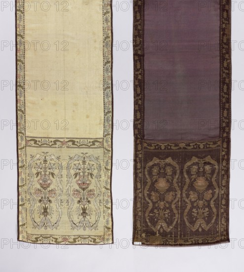 Kontusz belt, bipartite heads with motifs of elongated flower bouquets surrounded by a winding ribbon; still smooth, single-colored. Border with a floral tendril pattern. Colors: light straw, cream-silver, dark olive, sky blue, pink and brown-plum. At the bottom of one of the heads a preserved signature: BAREZ. 2nd half of the 18th century, Barysh Ukraine. National costume clothing accessory; length 297 cm, width 34.5 cm. Materials/technique: flower bushes/flower bouquets ornament, plant ornaments; men's fashion accessory kontusz belt., The image shows two long vertical fabric panels hanging side by side against a light background. The left panel is a pale cream color with a narrow decorative border in muted green, pink, and brown running along its edges and a patterned lower section featuring floral motifs in soft pink, green, and brown. The right panel is a deep brownish-purple with a darker brown ornamental border and a lower patterned area with stylized floral designs in shades of ...