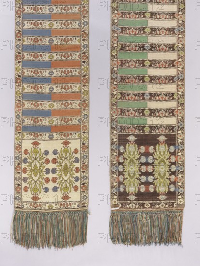 Kontusz belt; bipartite heads with a floral rosette pattern; alternating transverse stripes—plain and with a wispy floral ornament; sewn-on multicolored long silk fringe; predominant colors: sapphire blue, brick red, cream, and pink; 19th century; Poland; length 329 cm; width 29 cm; clothing accessory for national costume men's clothing accessory., Two long woven textile panels hang side by side against a pale background, each featuring a repeating horizontal stripe pattern alternating with decorative floral bands. The left panel shows stripes in muted blue and rust orange separated by cream bands with small floral motifs, a broader cream section near the bottom with mirrored floral medallions in green, blue, and rust, and a narrow floral border running along the panel edges; the right panel displays stripes in pale green and cream against a dark brown ground with floral bands, a darker lower section with large vertical floral medallions in green and pale blue and coral, and a similar ...