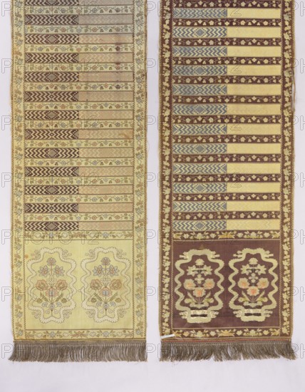 Kontusz belt;, Polish costumes; kontusz belts, men's clothing accessories; four-sided belt with bipartite heads patterned with stylized flower bouquets surrounded by a winding ribbon. Design includes transverse stripes alternating floral tendrils and geometric patterns, floral tendril edging, and sewn-on gold fringe. Predominant colors: light yellow, brown, salmon, blue, and green. 2nd half of the 18th century; Lyon, France. Length 441.5 cm; width 36 cm., The image shows two long woven textiles hanging side by side against a light background; the left textile is primarily pale yellow with patterns in brown, muted pink, blue, and green, featuring horizontal patterned bands above a section with two mirrored floral medallions and a fringed bottom edge, while the right textile is primarily brown with bands of yellow and blue zigzag and floral motifs, a lower section with two ornate floral cartouches in yellow and pink tones, and a fringed bottom edge.
