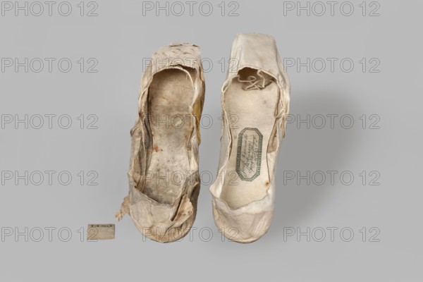 Flat women's slippers of white satin. Flat-cut toe, symmetrical soles of thin leather. The endpaper and back of the lining are made of white glacé leather, while the front is made of white canvas. On the endpaper there is an octagonal, elongated company label printed in green with the inscription: Józef Marczewski / in Warsaw / at Dluga Street / No. 543. Maker: Józef Marczewski Warsaw, shoemaker's workshop, ca. 1830–ca. 1840. Date: 1836. Place of origin: Warsaw. Function: women's footwear slippers, fashion accessory. Dimensions: height 5.2 cm, length 23.5 cm., A pair of worn fabric shoes placed side by side on a plain light gray background, one shoe showing a heavily tattered and discolored upper with frayed edges and a dirty interior, and the other shoe appearing less damaged with a cleaner interior and a small decorative label visible on the insole; the shoes display colors including off-white, beige, tan, gray, and hints of brown and yellow from stains and wear, and there is a small...