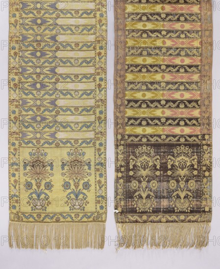 Kontusz sash, Paschalis Jakubowicz Manufactory Warsaw; belt manufacturer; 1788–1794. Bipartite heads with the pattern of elongated flower bouquets; transverse stripes with alternating floral and geometric ornamentation. Sewn-on silk fringe, beige. Colors: straw, pink, blue, light green. Four-sided sash with silk fringe. Polish kontusz sash men's national clothing accessory, length 272 cm, width 36 cm. Dated 1791–1794. Place of origin: Lipków. Maker: Jakub Paschalis Jakubowicz ?-1816/1817., The image shows two long woven textile panels hanging side by side, each with ornate horizontal patterned bands and decorative borders; the left panel is primarily pale yellow with accents of blue, light purple, brown, and cream, featuring floral motifs near the lower section and a fringe of pale yellow threads at the bottom, while the right panel is mainly darker with olive yellow, brown, pink, and cream tones, also displaying floral designs toward its lower area and a fringe of yellowish threads at...