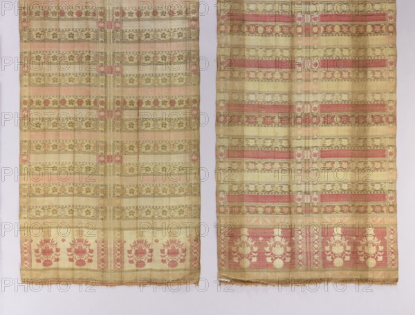 Kontusz belt, mid-18th century, probably Russian. Four-sided type. Materials/technique not specified. Design: four motifs in each head with heads divided in half; heads feature flower bouquets in vases/pots. Transverse stripes alternating plain and floral tendrils. Floral-tendril edging runs around the belt and twice in the middle, dividing the heads into two halves. Ornamentation: flowers, flower bouquets, flower bushes, plant tendrils, floral tendrils. Function: clothing/accessory, men's national costume accessory. Colors: black, red, pink, cream, brown. Dimensions: length 350 cm, width 50 cm., A pair of long rectangular woven textiles hung side by side against a pale background, each showing horizontal bands of decorative patterns and floral motifs. The fabrics display a muted palette of gold and beige as the dominant colors, with accents of faded pink and olive-green woven into stripes and ornamental designs. Both pieces feature repeating rows of small floral and geometric motifs a...