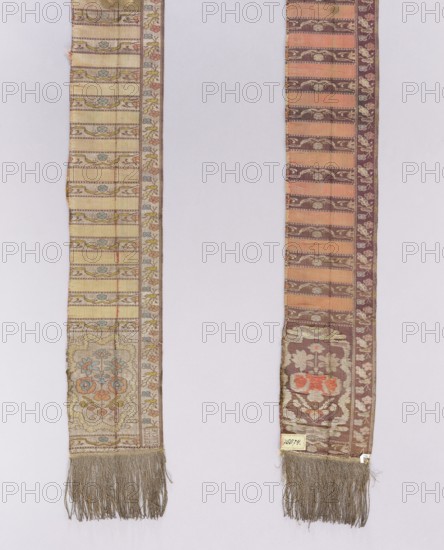 Half of a kontusz belt, woven by Jan Madzarski weaver; Sluck, ?-ca. 1800; manufactured by Karol Stanislaw Radziwill Manufactory Sluck; ca. 1767–1790. Metal threads; sewn-on silver fringe. Ornament: heads — a flower bush surrounded by a medallion of winding ribbon with small flower branches around the outer edge; center — transverse shelves alternating smooth and motifs of winding ribbon with flowers; borders — vertical floral branches; horizontal like a shelf with winding ribbon; borders also feature ladder and checkerboard motifs. Colors: recto — background of heads, borders, and shelves with tendrils silver, ornament in gold, sky blue, pink, and yellow-green; plain light pink shelves. Verso — background of heads, borders, and shelves with tendrils brown, ornament in silver and pink; smooth dark pink shelves. Weave density approx. 16/40 x2. Analogous flower-bush medallion motifs appear on other Slutsk belts. Date: ca. 1767–1780. Place of origin: Slutsk Grand Duchy of Lithuania / Polan...
