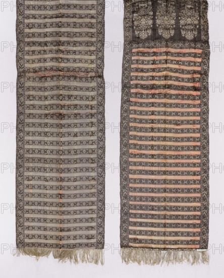 Kontusz belt, Polish men's costume accessory kontusz belt, sewn from pieces; 18th century. Materials and construction: sewn textile with sewn-on silver fringe. Origin: Constantinople Istanbul, Turkey. Dimensions: length 302.5 cm, width 31 cm. Ornament and design: triptych heads with three floral bouquet motifs in vases palmette-shaped bases; floral bouquet pattern. Center: alternating transverse stripes — smooth and with a floral tendril motif. Borders: floral tendril motif vertical borders with silhouetted tendril showing iris flowers. Patterns include double triangles and squares. Color scheme: silver, dark brown originally black?, and crimson-pink; descriptions note alternating use of silver and dark brown backgrounds and ornaments on heads, shelves, and borders. Style/notes: typical of Istanbul belts; notable carnation drawings in belt heads; tendril motifs related to Persian and Slutsk belt designs., A pair of long woven textile panels hung side by side against a pale background, ...
