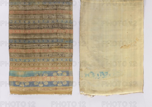 Kontusz belt, purchase provenance. Polish clothing; kontusz belt; men's fashion accessory. Tripartite heads with a rosette motif with carnation flowers around it; transverse stripes with a floral tendril motif in various colors separated by small stripes with a checkerboard motif; partial edging. Colors: blue, pink, beige, brown, ochre. 18th century, Russia place of origin. Length 250 cm; width 46 cm., The image shows two adjacent rectangular fabric panels laid flat on a pale background. The left panel features horizontal bands of patterned weave in muted shades of blue, pink, gold, beige, brown, and olive with floral and geometric motifs and a slightly worn, aged texture; the bottom edge is slightly frayed. The right panel is a mostly plain, light cream to pale yellow fabric with subtle vertical weave lines, a few irregular stains and a pale turquoise smudge near the lower middle, and a slightly ragged lower edge. The overall color palette includes cream, pale yellow, blue, pink, gold...