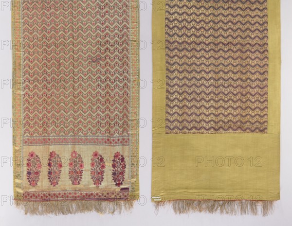 Kontusz belt. One-sided kontusz belt with five-part heads; head ornament consists of five bouquets in vases. Border of stripes: a wide central band with stylized flower ornament and narrower bands with geometric ornament. Fringe sewn on. Ornament of stylized small flowers enclosed in narrow zigzag stripes. Colors: gold, pink, green, silver, and blue. 18th century, India. Materials/technique: textile clothing accessory. Dimensions: length 417 cm, width 54.5 cm., Two adjacent patterned fabric panels hang side by side against a pale background; the left panel features a repeating chevron motif in muted beige and tan with accents of pink and green, bordered by a narrow decorative band and ending in a section with vertical floral sprays in shades of pink and red on a pale background, with a fringed lower edge in beige and gold; the right panel shows a larger field framed by a wide chartreuse border, the inner area displaying a repeating zigzag pattern in deep brown and gold with subtle pink...