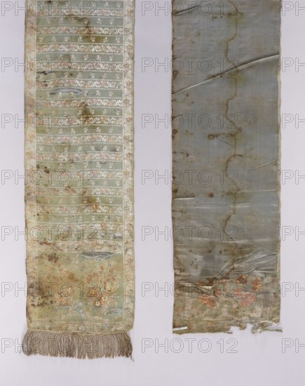 Kontusz belt, Royal Silk Manufactory in Grodno; silk fabric and belt manufacture; 1768–1780. Solid, reversible kontusz belt with sewn-on gold fringe. Heads: two asymmetrical floral bouquets floral branches arranged antithetically surrounded by ribbon festoons at the top and floral garlands at the bottom. Center: transverse shelves alternating motifs of floral projections and two intertwined ribbons fastened with flowers. Borders: vertical and horizontal floral twig motif with bends featuring small baskets with flowers; checkerboard border. Predominant colors: blue gray-blue background of heads and shelves, silver, salmon/pink, beige, brown, and green; silver background on the edges with similar ornament colors. Weave density approx. 44/25 x2. Flower-basket motifs on the edges are characteristic of belts from the Grodno workshop. Date: 1768–1780. Place of origin: Grodno Grand Duchy of Lithuania, Poland/Lithuania. Dimensions: length 344 cm, width 28 cm., Two long vertical fabric panels l...