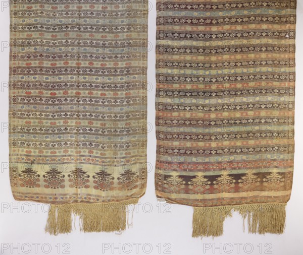 Kontusz sash, floral bouquets ornament, palmettes ornament, geometric ornaments, one-sided sash, floral ornaments, Polish sash, Polish costume accessory, kontusz sash, sash, Russia, fashion accessory, clothing accessory, men's clothing accessory, men's accessory. Five-part heads with an ornament of stylized, inverted floral bouquets, alternating transverse stripes with an ornament of small Persian palmettes, floral tendrils, and a fine wavy pattern. Silk fringe. Predominant colors: light yellow, brick red, brown, and sapphire blue. 18th century, Russia, national costume accessory. Length 331 cm, width 64.5 cm., The image shows two long woven fabric panels side by side, each with horizontal patterned stripes and decorative borders, both ending in fringed tassels; colors visible include beige, brown, cream, muted green, pale blue, soft red, and faded gold, with floral and geometric motifs repeated across the stripes and a row of larger stylized floral or tree-like designs near the lower ...