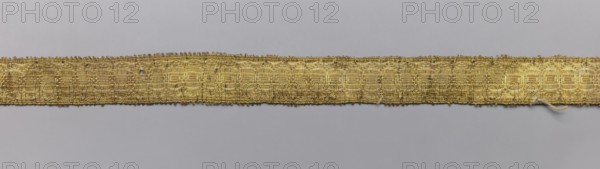 Five gallons, gallons haberdashery, origin unknown, geometric ornaments, 18th century, Europe, fabrics, width 1.5 cm, length 63 cm., A narrow woven trim runs horizontally across a plain background, showing a textured pattern of interlaced threads with a slightly irregular top edge and a few loose fibers along the lower edge; the trim appears in shades of gold and yellow with hints of darker brown in the weave, while the background is a smooth light gray.