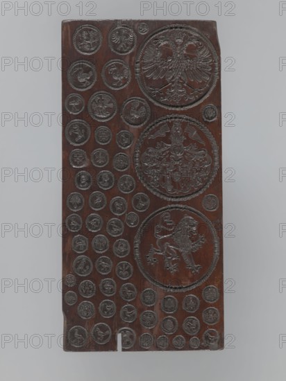 Gingerbread mold with 3 coats of arms and 52 medallions, boards and gingerbread; national emblems, zoomorphic motifs, coats of arms, banners, female busts; decorative art. Rectangular, flat gingerbread mold with representations forming medallions of various sizes, with a wreath-shaped border. Three large medallions, placed one below the other, contain heraldic images: 1. A double-headed eagle under a crown. 2. A quartered coat of arms with a lion, an eagle, a human figure, and the letter W in the fields; a human head in the central field; the shield topped with a crown, above which are a female bust and two banners; decorative lambrequins made of plant twigs flank the shield. 3. A mounted lion facing right. The form's decoration is complemented by 52 small medallions containing images of animals mostly birds, and anthropomorphic, geometric, and plant motifs. 16th–17th century, unknown locality; utility item., A vertical rectangular wooden panel with a dark brown surface carved with a g...