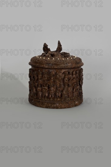 Wooden tankard, carved, probably a peg tankard, religious scenes, Gospel scenes, Resurrection of Christ iconography, inscriptions, vessels, Passion Bible; New Testament, human figures, figurative motifs, decorative art. Wooden pear-shaped tankard, so-called peg tankard, round, richly decorated with bas-reliefs depicting Passion scenes, with a Resurrection scene on the lid. The lid rim and handle are decorated with plant motifs and masks, and studded with ivory pins. In the center is a row of vertically driven metal pegs placed at regular intervals the top two are missing. 17th century, Scandinavia, vessel; height 23.5 cm, width 20.5 cm., A round carved wooden container with a lid sits against a plain light gray background; the container is dark brown with detailed relief carvings of human figures and ornamental patterns all around its sides, and the lid has carved decorative elements rising from its center and a ring of small pale beads around the top edge; the lighting creates soft sh...