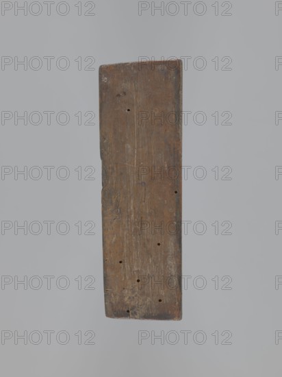 Double-sided gingerbread mold. Obverse: coat of arms with initials GG, top inscription Memento mori, two cherubs at the sides, bottom inscription DENATUS 23 May A 1700, laurel wreath. Reverse: intertwined monogram CMP, under a crown. Decorative crown with geometric and plant ornaments. Materials/function: gingerbread mold applied/decorative art, utility item. Motifs: wreath, Latin aphorisms, knotted monograms, plant ornaments, cartouches, angel with trumpet, epitaphs. Date: 1700. Dimensions: height 5 cm, width 15 cm, depth 12 cm. Role/classification of the creator: unknown., A single rectangular wooden plank is centered against a plain light gray background, showing a weathered surface with visible grain, scratches, and a few small round holes; the plank's colors include brown and darker brown tones with hints of gray and subtle lighter streaks, and its edges appear worn and slightly rounded.