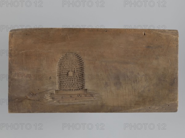 Gingerbread mold, double-sided. Obverse: image of a rider on a horse in a parade uniform from the Napoleonic Wars period, wearing a bicorn, caftan with epaulettes and braiding, an order on the chest, striped trousers and long boots; horse decorated with a geometric motif; bottom decoration of leaves and flowers. Reverse: small image of a beehive. Rectangular wooden mold, edge carved with the letters CG Gl. initials of the woodcarver or owner. Materials/technique: woodcarving for gingerbread molds; style: decorative/applied art; motifs: Napoleonic soldiers, riders, horse, floral decorations, historical military costume. Date: 18th–19th century. Place: Province of Silesia 1742–1918. Dimensions: height 51.5 cm, width 25.5 cm, depth 5 cm., A rectangular wooden board in shades of brown with a smooth, worn surface and visible wood grain, featuring a raised textured semicircular pattern near the center left composed of a honeycomb-like grid and a small arched cutout, a few shallow scratches a...