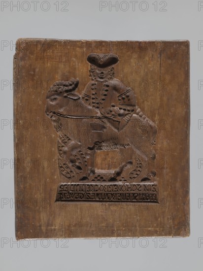 Double-sided gingerbread mould. Rectangular; obverse: man in 18th-century attire tricorn hat, justaucorps, culottes, long boots seated on a goat, carved inscription at the bottom: EIN SCHÖNER BOCK EIN GUTER / PFERD IST EINER GN ... DIE ZIGE WERT, with plant and floral ornament below; reverse: Adam and Eve in Paradise wearing leaf loincloths before the Tree of Knowledge with a coiled serpent; above them a bearded figure holding an orb probably God against a heavenly vault with sun, moon, and stars; animals around Adam and Eve include a cat, deer, bird, cow, and squirrel; composition surrounded by a round decorative frame decorated with a plant twig. Gingerbread mould, wood; 18th–19th century, Silesia Province, 1742–1918. Dimensions: height 21.4 cm, width 24 cm, depth 3.7 cm., A rectangular wooden panel with a carved relief of a person riding an animal; the panel shows visible wood grain and worn edges and is primarily brown with variations in darker and lighter brown tones, and the back...