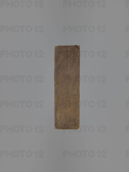 Double-sided gingerbread mould. Obverse: decorative pipe with fluted decoration, letter A in an oval on the stem, and two decorative tassels at the mouthpiece. Reverse: nine stylized fish covered with scales arranged in a row. Folk-style decorative applied art gingerbread mould. 18th–19th century, Province of Silesia 1742–1918. Form rectangular; height 22.7 cm, width 11.5 cm, depth 3.5 cm., A rectangular wooden block with worn, rounded edges suspended against a smooth gray background, the wood showing a brown, weathered surface with visible grain patterns and a few lighter spots and darker smudges.