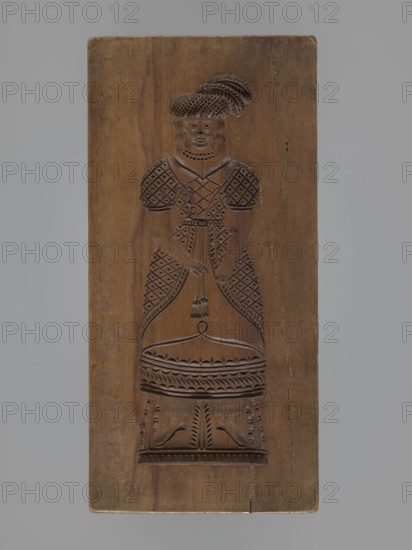 Double-sided gingerbread mould. Obverse: female figure in a long, patterned, richly decorated dress, wearing a hat decorated with an egretta. Reverse: male figure with a fur hat, dressed in a fur-lined coat over a shirt with decorative embroidery, holding a long pipe. Plant decoration at the bottom of both figures. Woodcarving, folk-style decorations; applied/decorative art; gingerbread moulds. 18th–19th century, Province of Silesia 1742–1918. Form: double-sided rectangular mould. Dimensions: height 19 cm, width 9 cm, depth 3.3 cm., A rectangular wooden panel carved in a brown wood tone shows a full-length figure of a person in relief, wearing a dress with patterned puffed sleeves and a fitted bodice, a hat with layered feather-like shapes, and a necklace; the figure's hands are clasped near the waist and a tassel-like detail hangs from them, and the carved skirt and lower section display repeated geometric and leaf-like motifs; the background surrounding the carving is plain wood with...