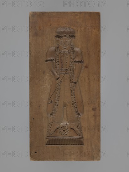 Double-sided gingerbread mould. Obverse: female figure in a long, patterned, richly decorated dress, wearing a hat decorated with an egretta. Reverse: male figure with a fur hat, dressed in a fur-lined coat over a shirt with decorative embroidery, holding a long pipe. Plant decoration at the bottom of both figures. Woodcarving; folk-style decorations; applied/decorative art; female and male figures; historical costumes; water pipes. 18th–19th century, Province of Silesia 1742–1918. Double-sided rectangular mould. Height 19 cm, width 9 cm, depth 3.3 cm., A carved wooden panel showing a full-length figure in relief standing on a decorated rectangular base; the figure has long curled hair or braided detailing, a round hat or headpiece, and wears a long garment with decorative edging and textured patterns; the figure’s arms are bent at the elbows with hands held near the waist, and a thin carved element extends diagonally across the torso; the panel surface shows natural wood grain, small ...