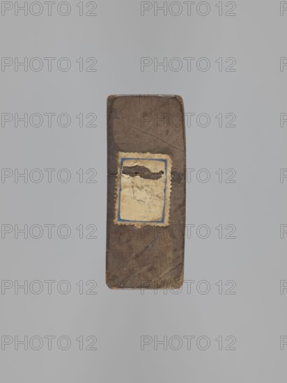 Double-sided gingerbread mold. Obverse: couple holding hands — a woman in a richly decorated long dress with a hat and a man in a caftan and short wig, both in costumes typical of the 18th century; decoration of plant elements at the bottom. Reverse: three empty rectangles. Woodcarving; applied art; genre scenes, female figures, male figures, couples in love, plant motifs. Rectangular. 18th–19th century, Province of Silesia 1742–1918. Height 20 cm, width 8.7 cm., A rectangular wooden object with rounded corners is shown against a gray background, the wood appearing brown with darker brown grain, scratches, and a few cracks; a worn rectangular paper label with a scalloped edge is affixed near the center, the label showing beige, off-white, and a faded blue border and areas of darker brown discoloration.
