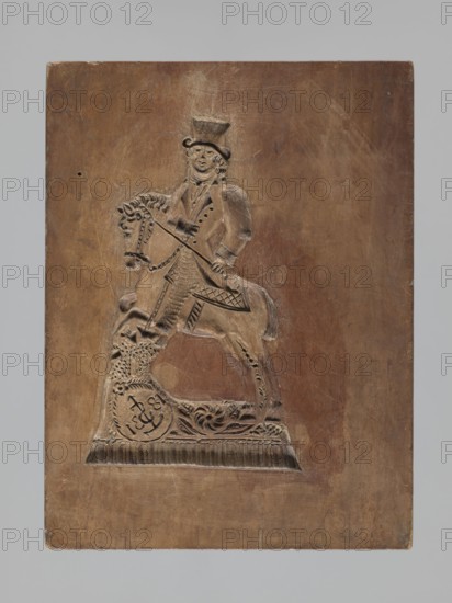 Double-sided gingerbread mould. Rectangular wooden form; obverse: image of a lion with abundant mane, standing on a base decorated with plant-twig ornament, holding a ball engraved with the date 1829 and a symbol of an anchor intertwined with the letter S; bottom with floral and plant decoration. Reverse: figure of a cavalier on horseback in early 19th-century riding attire jacket, breeches, top hat, holding a riding crop; at the horse's front legs a round shield engraved 1831 and the same anchor-with-S symbol mark of the woodcarver or owner; bottom with floral and plant ornament. Materials: wood gingerbread mould; subject matter: rider on a horse, lion, figurative scenes, plant motifs; style: applied folk/culinary mould; date marks: 1829 and 1831; region: Silesia Province of Silesia, 1742–1918. Dimensions: height 25.8 cm, width 19.4 cm, depth 4.3 cm., A rectangular wooden panel with a carved relief of a mounted figure occupies the center; the panel shows a warm brown wood tone with li...