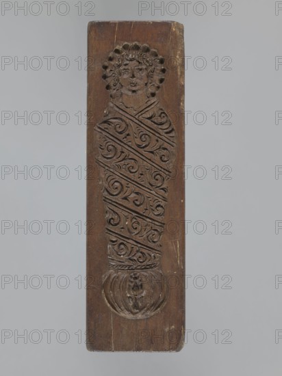 Double-sided gingerbread mold — obverse: female figure; reverse: baby in swaddling clothes. Woodcarving, gingerbread mold, applied/decorative art. Single-sided rectangular mold with an image of a female figure in Silesian folk costume: bonnet, large bow tied under the neck, long dress with short puffed sleeves, decorated at the bottom with floral and plant ornament; figure holds a basket with flowers. Other side shows a baby in decorative swaddling clothes. Folk-style decorations, floral motifs. 18th–19th century, Province of Silesia 1742–1918., A vertical rectangular wooden block with a carved relief of a stylized human figure; the wood is brown with areas of lighter wear and small scratches, and the background around the block is a neutral gray. The carved figure shows a rounded head with curly hair and facial features, a long wrapped body decorated with a repeating swirling foliate pattern carved in diagonal bands, and a rounded carved base with a small decorative motif; the carved ...