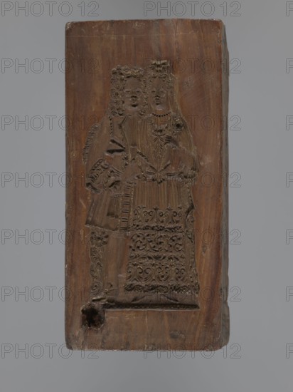 Double-sided gingerbread mould. Obverse: Madonna and Child with a crown, in a long patterned dress, surrounded by a double oval inner frame forming tongues of flame and an outer laurel-wreath frame. Reverse: two standing figures man and woman in courtly costumes of the 17th–18th centuries — the man with a long wig, justaucorps, culottes and stockings; the woman with a wig and a long dress with a low neckline, decorated at the hem with a plant tendril. Plant ornaments and religious motifs. Material: gingerbread mould applied art. Date: 18th–19th century. Region: Province of Silesia 1742–1918. Form: rectangular. Dimensions: height 20.3 cm, width 10 cm, depth 3.5 cm., A vertically oriented rectangular wooden block with a carved raised design of a couple standing side by side, the carving showing textured patterns and ornamental details on their clothing and hair; the wood displays a natural brown color with varying darker and lighter brown tones and a few small worn areas and scratches, w...