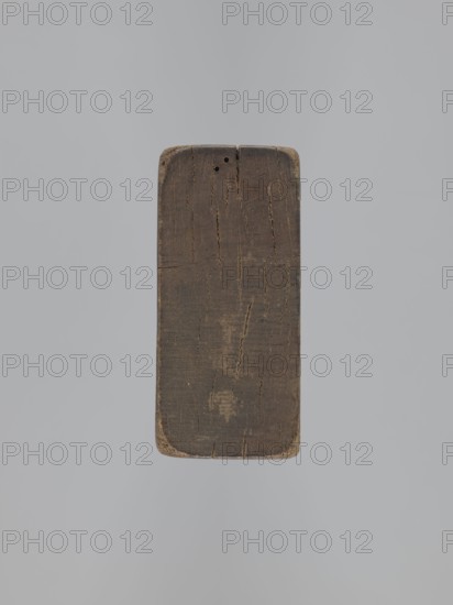 Double-sided gingerbread mold. Obverse: baby in swaddling; Reverse: baby in swaddling. Folk-style decorations with geometric and floral ornament; decorative frame around the figure. Rectangular mold, applied art, souvenir. 18th–19th century, Province of Silesia 1742–1918. Mold. Height 16.8 cm; width 7.8 cm; depth 3.7 cm., A rectangular block of weathered wood with rounded corners is centered on a plain light gray background; the wood shows a dark brown surface with lighter brown worn areas, visible cracks and grain lines, and a few small holes near one end, with edges showing lighter beige wear.