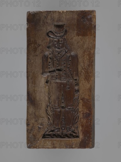 Double-sided gingerbread form. Side A: figure of a bachelor; Side B: grapevine with a large grape bunch., woodcarver or gingerbread maker. Materials/subject: fruit ornament, gingerbread, decorative art, customs, male figures, souvenirs, plant motifs, applied art, historical costumes, grapevine iconography, folk motifs. Description: rectangular form; one side shows a long-haired male figure with a high hat in a bachelor’s costume from the turn of the 18th and 19th centuries, wearing a justicorn and culottes with stockings, standing among decorative foliage; the other side a large grape bunch. Date: 1796. Place/region: Silesia Prussia; 1742–1918. Object type: form. Dimensions: height 14.3 cm, width 7.2 cm, depth 2.7 cm., A rectangular carved wooden plaque showing a carved full-length figure in relief, with a carved hat, long hair, a jacket with detailed buttons, a vest, trousers, and boots, standing on a carved base with decorative foliate elements; the wood surface shows worn and smooth...