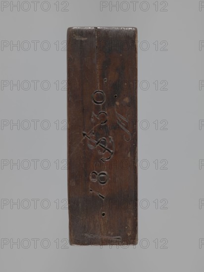 Double-sided gingerbread form. Side A: female figure; Side B: baby in swaddling clothes. Maker unknown woodcarver or gingerbread maker. Gingerbread, decorative/applied folk art; Silesian Province of Silesia, 1742–1918. Rectangular form: one side shows a standing woman with a headscarf, leaning on a ladder and holding a broom; the other shows a swaddled baby decorated with a geometric ornament. On one edge the date 1830 is engraved with the letter S against an anchor background and below it the letter M mark of the maker. Date: 1830. Materials: gingerbread form wood. Dimensions: height 13.5 cm, width 6.5 cm, depth 4.5 cm., A vertically oriented rectangular block of wood with a dark brown surface showing a vertical seam near the top and worn edges, featuring a few shallow carved indentations and scratches across its face, with small round holes visible and areas of lighter brown wear; the background is a uniform light gray.