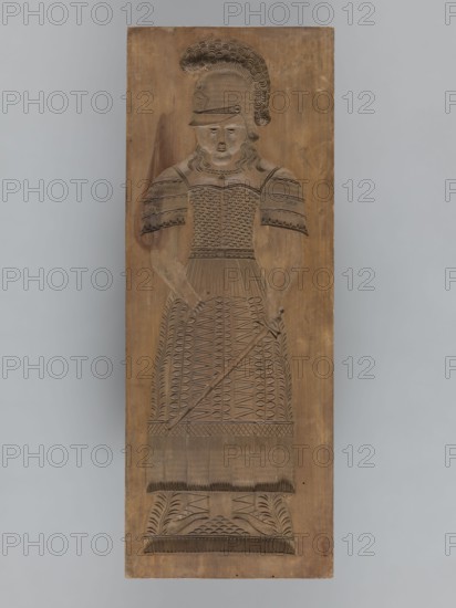 Double-sided gingerbread form: obverse — female figure in a helmet; reverse — male figure in a helmet. Gingerbread mold, applied/decorative art; militaria, historical costumes, plant ornaments, armour, swords. Double-sided rectangular form: one side shows a female figure in a long patterned dress with a neckline, wearing a helmet with a plume, holding a sword in one hand and a roll of paper in the other, wearing shoes, with a plant ornament at the bottom. The other side shows a male figure in armor resembling Roman legionary or Greek hoplite armor, with a similar plumed helmet, holding a shield bearing two crossed swords and a crown, and a javelin in the other hand; a sword is girded at his side, he wears sandals, with a plant ornament at the bottom. 18th–19th century, Silesia Province 1742–1918. Form; height 59 cm, width 22 cm, depth 4.5 cm., A carved wooden panel depicts a standing figure in relief wearing a helmet with a plume and an intricately patterned dress or armor, holding a l...