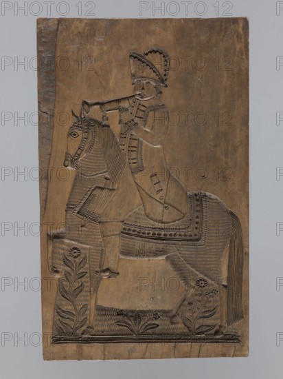Double-sided gingerbread form. Obverse: image of a rider; reverse: four representations of human figures. Double-sided rectangular form; on one side an image of a trumpeter on a horse dressed in a decorative tail, in a costume from the turn of the 18th and 19th centuries—long jerkin with wide tails, breeches and long boots, tricorn hat—with floral decoration at the bottom. Second side: four small images of human figures shown from front and back: first, male, carrying a basket filled with children probably the folk Kinderbringer; second, female in a high headdress and country dress, holding a handkerchief and a small basket. Gingerbread form; genre scenes, decorative folk motifs, riders, trumpeters, floral and plant ornaments. 18th–19th century, Province of Silesia 1742–1918. Height 42 cm, width 25.5 cm, depth 2.8 cm., A carved wooden panel depicting a figure riding a horse, both rendered in low relief with incised patterns; the rider wears a tall, decorated hat and a long garment with...