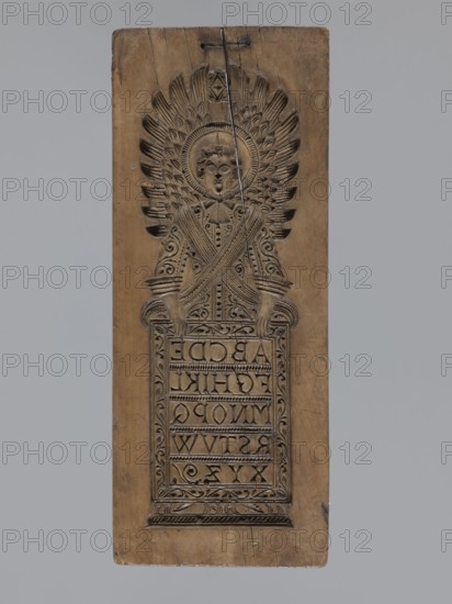 Double-sided gingerbread form. Obverse: figure of an angel with the alphabet. Reverse: various floral ornaments. Double-sided form with a rectangular shape; on one side a male figure probably an angel in a standing position, in a costume richly decorated with plant ornament, girded with two sashes, holding a decorative board with the alphabet inscribed on it; above the figure's head a halo; in the background a feather and flame motif angel wings?. The other side: rectangular field filled with floral and plant decoration, among which the head of a baby. At the top a signature: initials G and R mark of the woodcarver or gingerbread maker/owner of the workshop. 18th–19th century, Province of Silesia 1742–1918. Material: form. Height 32.3 cm; width 13 cm; depth 2 cm., A rectangular carved wooden panel with a carved figure in relief occupying the upper portion and a framed rectangular carved panel below; the figure has a round halo-like disk behind the head and a stylized face with carved h...
