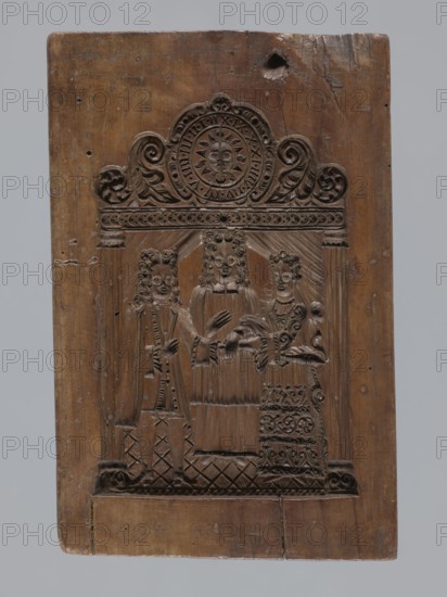 A single-sided gingerbread mould with a wedding ceremony scene, figurative scenes, gingerbread mould, weddings, male figures, female figures, volutes, folk-style decorations, plant motifs, gingerbread, Silesia Province of Silesia; 1742–1918, decorative art, folk motifs. A single-sided rectangular mould with a wedding scene: in the centre a priest dressed in a chasuble, wearing a wig; to his left a man and to his right a woman with their hands joined by the priest. Both wear richly decorated turn-of-the-17th/18th-century costumes and wigs — the man in a justaucorps, culottes and stockings, the woman in a long patterned dress with a low neckline. Above the heads of the figures is a decorative finial supported by two columns; its central element is a round clock face showing a sun with a human face surrounded by volute and plant ornament, hands on the face, and a rim marked with Roman numerals. Date: 18th–19th century. Dimensions: height 23 cm, width 15.5 cm, depth 4.5 cm., A rectangular ...