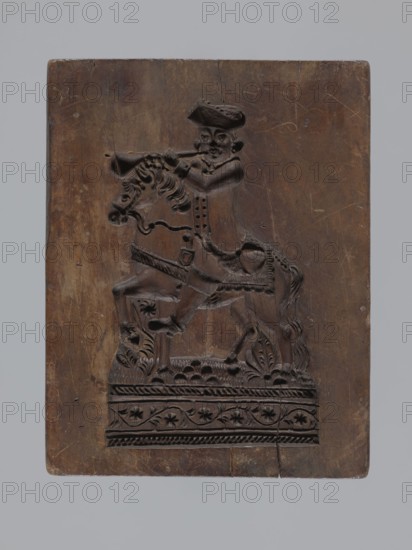 Double-sided gingerbread mould with the image of a rider on both sides, woodcarver or gingerbread maker; gingerbread mould; figurative scenes of riders and male figures on horses; plant motifs and folk-style decorations; applied decorative art; Silesia Province of Silesia, 1742–1918. Double-sided rectangular mould: one side shows a rider-trumpeter in a tricorn hat in 17th–18th-century costume long caftan, breeches, long boots seated on a horse with decorative tack, both on a base with plant and geometric ornament; reverse shows another rider probably a hussar wearing a high mirliton cap and a fur-lined jacket, with geometric and floral ornament at the bottom. One edge engraved with the date 1797 and a central mark of the letter S against an anchor mark of the woodcarver or owner of the mould. Date: 1797. Type: mould. Dimensions: height 19 cm, width 15 cm, depth 5.5 cm., A rectangular wooden panel with a carved relief of a person riding a horse; the panel is mostly brown with darker bro...