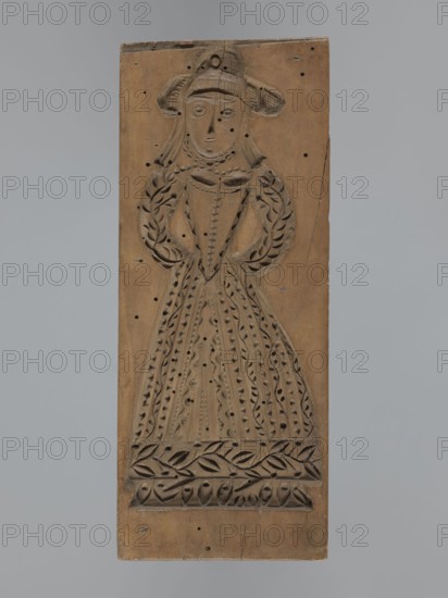 Double-sided gingerbread form. Obverse: female figure in a hat and long patterned dress; Reverse: baby in swaddling clothes richly decorated with geometric and plant ornament. Rectangular shape; folk motifs and plant ornaments; decorative art. 18th–19th century, Province of Silesia 1742–1918. Form. Height 23.5 cm, width 9.5 cm, depth 2.6 cm., A rectangular wooden panel carved in brown shows a stylized female figure in relief wearing a wide-brimmed hat and a long, patterned dress, with carved decorative leaf-like motifs around the skirt and along a horizontal band near the bottom; the figure has a simple face with circular eyes and a small nose, a necklace, and braided or tasseled details at the shoulders, and the panel surface has several small dark holes and slight cracks.