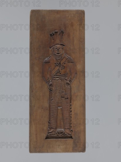 Double-sided gingerbread mould. Side A: figure of a soldier; Side B: various floral and geometric ornaments., woodcarver or gingerbread maker. Folk-style decorations; woodcarving; applied and decorative art; gingerbread moulds; male figures; military uniforms; folk motifs. Double-sided rectangular mould: one side shows a male figure in a Napoleonic-era military uniform, wearing a high headgear with a feather, numerous chest decorations, and a plant ornament at the bottom; the other side shows a rich floral and plant ornament enclosed in a tripartite frame with decorative spoked wheels in the four corners. On one edge an engraved date 1810 appears, with the letter S between the digits against the background of an anchor the maker's mark. Date: 1810. Place: Province of Silesia 1742–1918. Object type: form. Dimensions: height 31.7 cm; width 12.5 cm; depth 2.4 cm., A rectangular wooden panel with a carved standing figure in relief occupies the center; the panel is brown with variations in ...