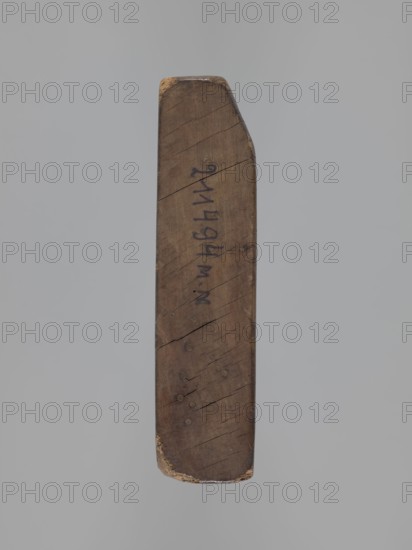 Double-sided gingerbread mould. Obverse: board with letters of the alphabet. Reverse: image of a running wild boar across a meadow. Double-sided rectangular mould; on one side a decorative board with the letters of the alphabet carved on it; the other side: image of a wild boar running across a meadow. On one of the edges there is a date engraved: 1806, between the digits of the date the letter S on the background of an anchor the mark of the woodcarver or gingerbread maker - the owner of the form. Materials/function: form for gingerbread; folk-style decorations; iconography includes wild boar and alphabet. Date: 1806. Place/region: Province of Silesia 1742–1918. Dimensions: height 16 cm, width 12 cm, depth 3 cm., A single elongated wooden object with a tapered end suspended against a neutral gray background, showing a weathered brown surface with visible wood grain, small cracks, and several round indentations; the top and bottom edges show worn areas with lighter beige exposed wood, ...