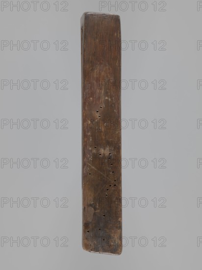 Double-sided gingerbread form; obverse: image of Madonna and Child, reverse: two rectangles with floral ornaments. Double-sided rectangular form; on one side a figure of the Virgin Mary in a large patterned robe, surrounded by children—two sitting on her lap, the other three at her feet—with a German inscription at the bottom: DIE LIEBE IS BEI MIR SO GROS ACH NIM / MICH IN DEINEM SCHOS. The other side features two long rectangular frames filled with floral ornament. Gingerbread mold, decorative folk motifs, religious iconography Madonna, Christianity. 18th–19th century, Silesia Province of Silesia, 1742–1918. Height 19 cm, width 11 cm, depth 3.3 cm., A long narrow wooden object with a rectangular cross-section shown vertically against a pale gray background, the wood surface is dark brown with lighter brown and tan worn areas, small scattered round holes and some scratches visible, the top edge is slightly rounded and the bottom edge is more blunt and worn, the wood grain and patchy di...
