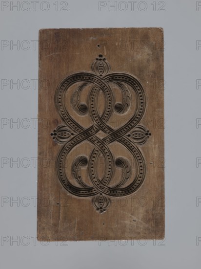 Double-sided gingerbread mould with a plant and floral ornament on both sides;, Materials and techniques: gingerbread usage, woodcarving; folk-style decorations with plant twigs, geometric motifs, and plant motifs. Description: rectangular double-sided mould — one side shows an elaborate ornament of plaiting with plant and geometric elements; the other side displays a similar decorative motif of two ribbons intertwined in figure-eights filled with and surrounded by lanceolate leaves. Date: 18th–19th century. Region: Province of Silesia 1742–1918. Dimensions: height 14.5 cm, width 8.5 cm, depth 1.7 cm., A rectangular wooden panel with a carved symmetrical looping design occupies the center, showing a dark brown carved pattern against a lighter brown wood surface; the carving features interlaced rounded loops with dotted borders and leaf-like motifs, and small rounded decorative elements at the top, sides, and bottom; the wood shows scratches, small holes, and worn areas; the background ...