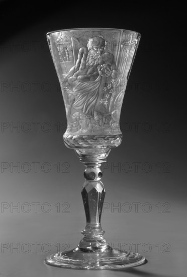 Chalice, glass, 1736–1744. Naliboki, Belarus Grand Duchy of Lithuania. Height 17.2 cm; width 7.7 cm. Round foot, slightly raised, trace of adhesive. Baluster stem, solid, faceted, separated from the foot by two plates with a ring, one of them with a flower; separated from the bowl by two plates of different diameter and a knob. Conical bowl, twice puffed out at the base, cut into rows of lenses. Engraved decoration all over the bowl, biaxial: seated Saint Hieronim Saint Jerome holding a skull, with a lion at his feet, in a room with bookcases, a table at the side; on the other side an inscription: THE LORD'S GIFT OF HIS LIFE / FROM WHICH HE MAKES / THE PRINCE OF SACRIFICES / MAY THE HOUR Strike for so many prosperous years / HOW MANY DROPS IN THE GOBLET / WHAT WINE IS IN THE WINE. Foot with a wide strip bearing a geometric pattern. Dedications; religious scenes; Hieronim Florian 1715–1760; Radziwill family; skull anatomist., A tall, clear glass goblet with an intricately carved bowl sh...