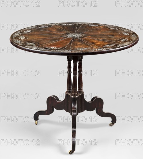 Table with round, tilting top on a shaft composed in the middle of three balusters, forked at the bottom into a tripod; inlaid with silver sheet. Plastic, sinuously curved legs on brass rollers, set in a cube with a wavy outline, supporting baluster columns, on which a similar cube with arcades at the bottom. Base veneered with rosewood and decorated with inlaid silver-sheet veins. Top veneered with mahogany on both sides, richly inlaid: a central enclosed plant twig with radiating veins defining a 12-pointed rosette, with oval medallions at the ends of the arms. Medallions filled with eagles with spread wings and, in every third case, a pair of antithetically positioned griffins, surrounded by plant ornament. Edge of the top decorated with acanthus leaves and palmettes. Top mounted on a square plate with a steel hinge not original, with a brass rotating two-armed latch. Styles: Empire, Biedermeier; motifs: griffins, arabesque, palmettes, eagles, acanthus twig. Date: 1835–1845. Place o...
