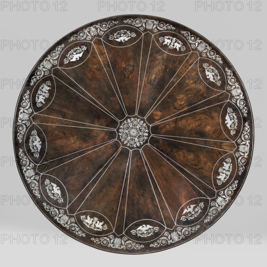 Table with round tilting top on a shaft composed in the middle of three balusters, forked at the bottom into a tripod; inlaid with silver sheet. Sinuously curved legs on brass rollers, set in a cube with a wavy outline, supporting baluster columns, on which a similar cube with arcades at the bottom. Base veneered with rosewood and decorated with inlaid silver-sheet veins. Top veneered with mahogany on both sides, richly inlaid: a central enclosed plant twig with radiating veins defining a 12-pointed rosette, with oval medallions at the ends of the arms. Medallions filled with eagles with spread wings and, in every third case, a pair of antithetically positioned griffins, surrounded by plant ornament. Edge of the top decorated with acanthus leaves and palmettes. Top mounted on a square plate with a steel hinge not original, with a brass rotating two-armed latch. Empire / Biedermeier style; decorated with griffins, arabesque, palmettes, eagles, acanthus twig. Possibly Poland, c. 1835–184...