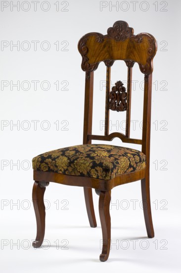 Chair, plant decoration, acanthus ornament, Louis Philippe style, mahogany chair with a padded seat and a high openwork backrest, with carved decoration. Square legs, S-shaped at the front with volute feet, and arched rear legs. Wavy frame with rounded front corners, with a seat in the form of an overlay cushion. The backrest is framed on the sides by straight stiles extending the rear legs, topped with a board with a symmetrical, wavy-cut outline, accentuated by carved acanthus appliqués. The filling has two straight stiles covered with astragalus, topped and fastened together with acanthus leaf arrangements, and a narrow lower stile, arched between the stiles. 1850–1860, Poland, possibly Warsaw. Seating furniture; height 118.5 cm, width 51 cm, depth 53 cm., A wooden chair with a carved backrest showing ornate scrollwork and a decorative central carved motif, a patterned upholstered seat with floral designs, and cabriole front legs and straight rear legs; visible colors include brown ...
