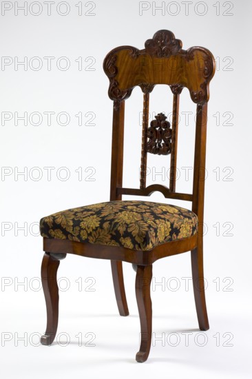 Chair, acanthus ornament, plant decoration, Louis Philippe style, mahogany chair with a padded seat and a high openwork backrest, with carved decoration. Square legs, S-shaped at the front with volute feet, and arched rear legs. Wavy frame with rounded front corners, with a seat in the form of an overlay cushion. The backrest is framed on the sides by straight stiles extending the rear legs, topped with a board with a symmetrical, wavy-cut outline, emphasized by carved acanthus appliqués. The filling has two straight stiles covered with astragalus, topped and fastened together with acanthus leaf arrangements, and a narrow lower stile, arched between the stiles. 1850–1860, Poland, possibly Warsaw, seating furniture, furniture; height 118.3 cm, width 50.8 cm, depth 54.5 cm., A wooden chair with a carved backrest and turned vertical supports, finished in a warm brown tone, features ornate scrollwork at the top and a carved floral motif in the center of the back; the seat is upholstered in...