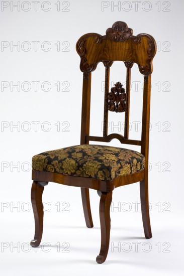 Chair, mahogany chair with a padded seat and a high openwork backrest, with carved decoration. Square legs, S-shaped at the front with volute feet, and arched rear legs. Wavy frame with rounded front corners, with a seat in the form of an overlay cushion. The backrest is framed on the sides by straight stiles extending the rear legs, topped with a board with a symmetrical, wavy-cut outline, emphasized by carved acanthus appliqués. The filling has two straight stiles covered with astragalus, topped and fastened together with acanthus leaf arrangements, and a narrow lower stile, arched between the stiles. Acanthus ornament, plant decoration, Louis-Philippe style, 1850–1860, Poland, possibly Warsaw, seating furniture, furniture; height 118 cm, width 51 cm, depth 54 cm., A wooden chair with a carved decorative backrest and turned vertical supports, featuring ornate scrollwork and a carved central medallion, a patterned upholstered seat with a floral design, and curved front legs; visible c...